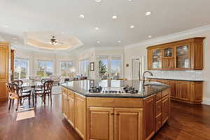 Kitchen featuring dark wood finished floors, dark stone countertops, gas cooktop, a sink, and a kitchen island with sink