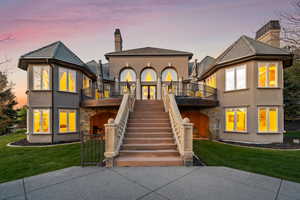 Back of property at dusk featuring a chimney, a yard, a balcony, and stucco siding
