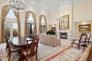 Dining room with a high ceiling, a high end fireplace, beamed ceiling, crown molding, and a notable chandelier