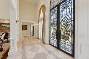 Foyer entrance with ornate columns, ornamental molding, french doors, a decorative wall, and wainscoting