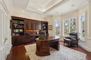 Office space featuring dark wood-style floors, crown molding, built in desk, a tray ceiling, and visible vents