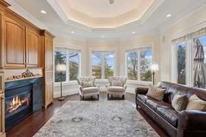 Living room with ornamental molding, a raised ceiling, a high end fireplace, and dark wood-style flooring