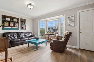 Living area featuring wood finished floors, crown molding, visible vents, and baseboards