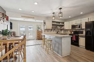 Kitchen with open shelves, black appliances, a breakfast bar area, backsplash, and light countertops