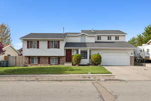 View of front of property featuring concrete driveway, fence, brick siding, a front lawn, and a garage