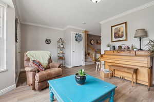 Living room with light wood finished floors, ornamental molding, stairs, and baseboards