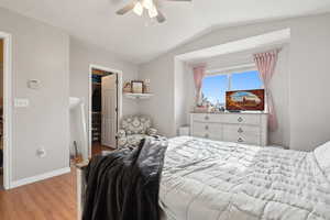 Bedroom with light wood finished floors, a closet, a walk in closet, baseboards, and lofted ceiling