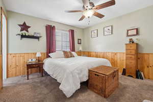 Carpeted bedroom with wooden walls, ceiling fan, and wainscoting