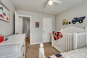 Carpeted bedroom featuring a nursery area, baseboards, and ceiling fan