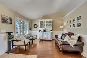 Living area with vaulted ceiling, dark wood-style flooring, a wainscoted wall, and crown molding