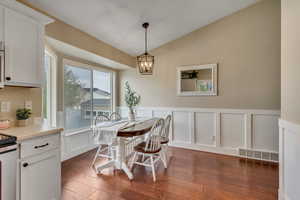 Dining area with vaulted ceiling, a decorative wall, wainscoting, visible vents, and dark wood-style floors