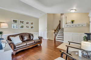 Living room with wainscoting, lofted ceiling, wood finished floors, stairway, and a decorative wall