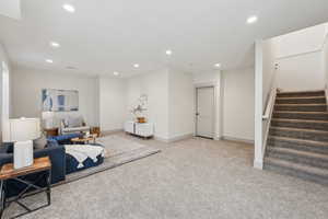Completed basement living area featuring recessed lighting, stairway, light carpet, and baseboards