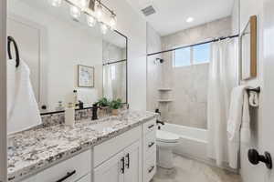 Full bath with vanity, toilet, marble finish floor, visible vents, and shower / tub combo with curtain