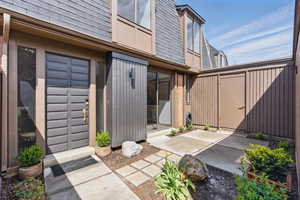 Doorway to property with a patio, brick siding, a shingled roof, and mansard roof