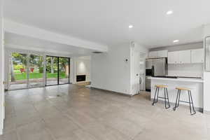 Kitchen with recessed lighting, a large fireplace, white cabinetry, baseboards, and open floor plan