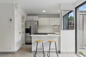 Kitchen with a breakfast bar area, light countertops, stainless steel refrigerator with ice dispenser, a peninsula, and backsplash
