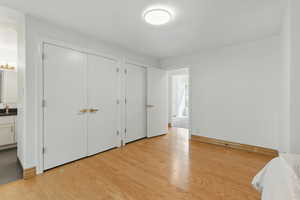 Unfurnished bedroom with light wood-style floors, ensuite bath, and baseboards