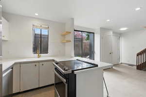 Kitchen featuring open shelves, appliances with stainless steel finishes, light countertops, a sink, and a peninsula
