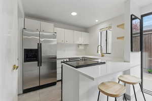 Kitchen featuring decorative backsplash, a breakfast bar area, stainless steel fridge with ice dispenser, white cabinetry, and a peninsula