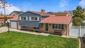 View of front of home featuring brick siding, fence, metal roof, a front yard, and concrete driveway