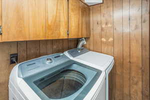 Washroom featuring wood walls, cabinet space, and independent washer and dryer