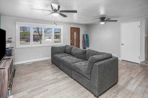 Living area with baseboards, a ceiling fan, a textured ceiling, and light wood-style flooring