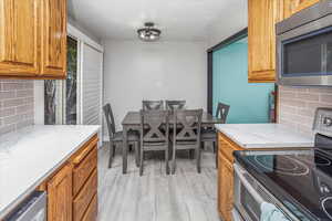 Kitchen with brown cabinets, appliances with stainless steel finishes, decorative backsplash, and light wood-type flooring