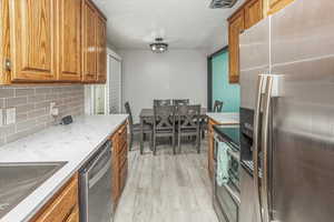 Kitchen with light wood finished floors, brown cabinetry, tasteful backsplash, light stone counters, and appliances with stainless steel finishes
