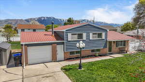 Split level home with metal roof, a mountain view, driveway, brick siding, and an attached garage