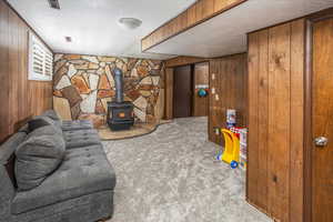 Interior space with wood walls, a textured ceiling, carpet flooring, and a wood stove