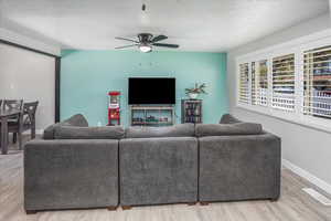 Living room with a ceiling fan, visible vents, baseboards, a textured ceiling, and wood finished floors