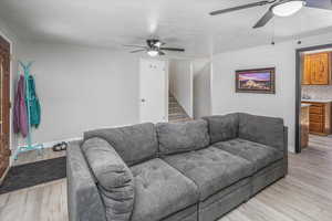 Living area with stairway, light wood-type flooring, a ceiling fan, and baseboards