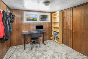 Carpeted office space with wood walls and a textured ceiling