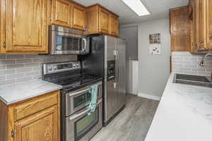 Kitchen featuring a sink, brown cabinetry, light wood-type flooring, a textured ceiling, and appliances with stainless steel finishes