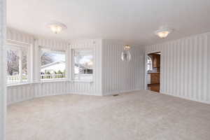 Unfurnished living room featuring visible vents, wallpapered walls, carpet flooring, and a textured ceiling