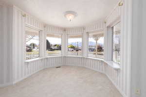 Unfurnished sunroom with wallpapered walls, carpet, a textured ceiling, and visible vents