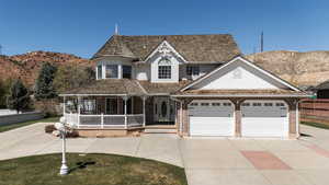 Victorian home with concrete driveway, an attached garage, a porch, brick siding, and a mountain view