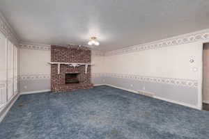 Unfurnished living room featuring a fireplace, a textured ceiling, visible vents, and carpet flooring
