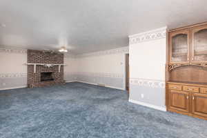 Unfurnished living room featuring a fireplace, a textured ceiling, visible vents, and carpet flooring