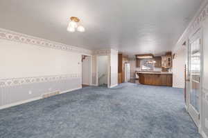 Unfurnished living room with carpet flooring, a textured ceiling, and wallpapered walls