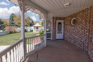 Doorway to property featuring covered porch, brick siding, and a yard