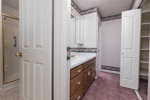 Full bathroom featuring a shower stall, a walk in closet, vanity, and a textured ceiling