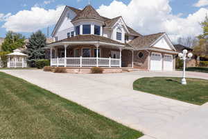 Victorian-style house with a gazebo, a front lawn, driveway, covered porch, and brick siding