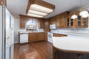 Kitchen featuring brown cabinets, light countertops, white appliances, glass insert cabinets, and dark wood-style flooring
