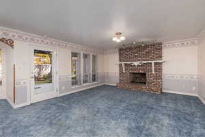 Unfurnished living room with a fireplace, a textured ceiling, carpet flooring, and ornamental molding