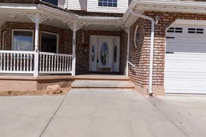 Entrance to property featuring brick siding, an attached garage, and covered porch