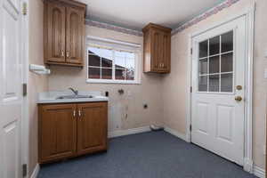 Washroom featuring a sink, electric dryer hookup, cabinet space, baseboards, and dark colored carpet