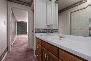 Bathroom with wallpapered walls, vanity, and a textured ceiling