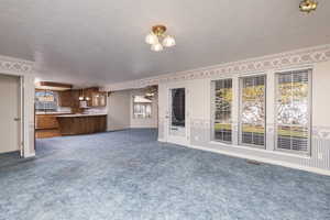 Unfurnished living room featuring wallpapered walls, a textured ceiling, plenty of natural light, and dark carpet